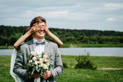 The first meeting is newlyweds on a green field outdoors. Bride goes back to the groom, surprise in nature. The woman closed her eyes to her husband. Happy wedding day of marriage.