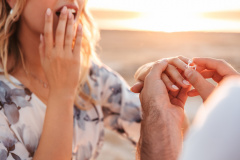 Cropped photo of caucasian man putting engagement ring on woman's finger while walking on beach